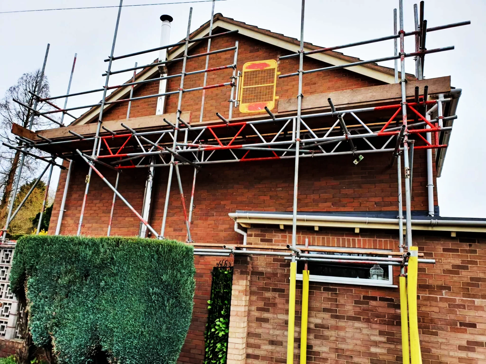 Scaffolding with red guardrails at the gable end of a brick house