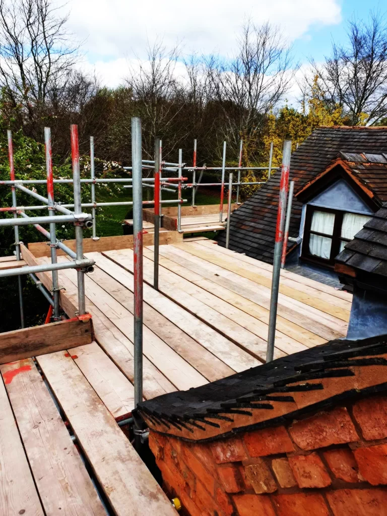 Boarded scaffolding platform at roof level beside a tiled roof